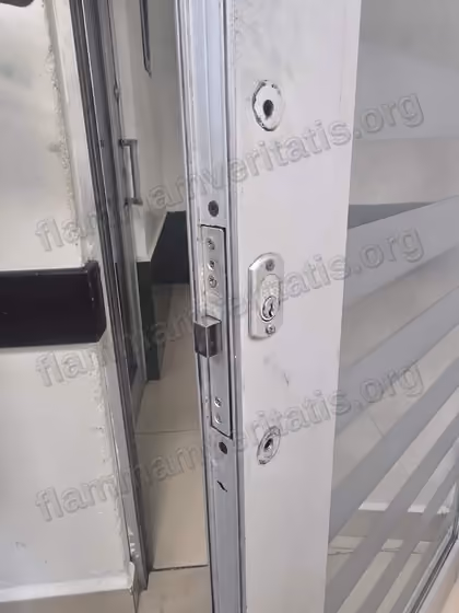 Canto de una puerta corrediza de vidrio y aluminio en el aula 2107, edificio 2, con una chapa de seguridad y dos orificios de montaje vacíos, sin manija instalada.