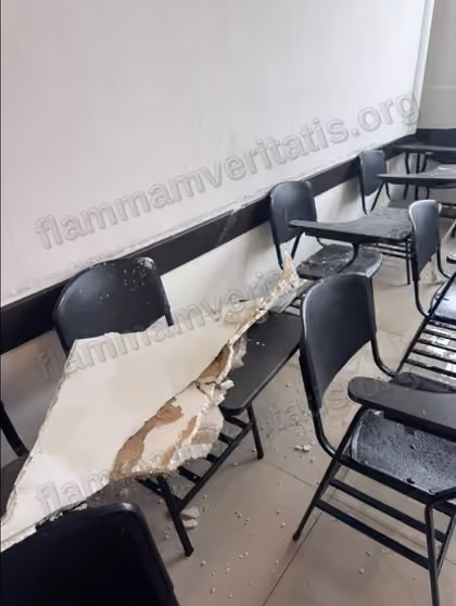 Trozo de aplanado de techo, partido y con escombro, caído sobre el respaldo y el paletero de una banca del aula 2301, con fragmentos de material dispersos en el piso y sobre otras bancas cercanas.