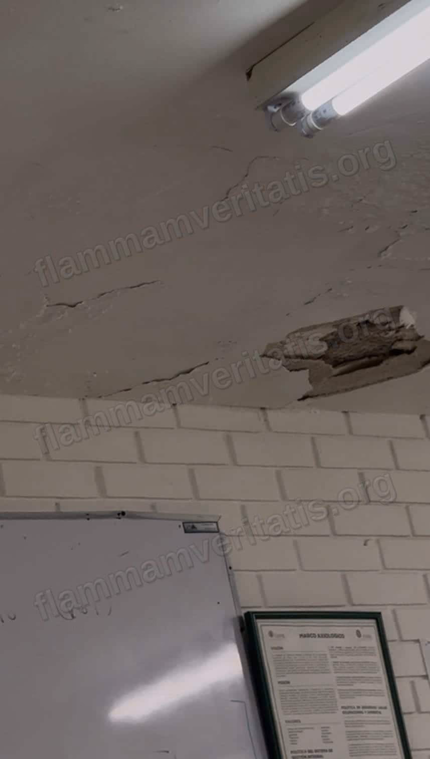Techo del aula 3301 con una grieta grande y un trozo de aplanado desprendido junto a una lámpara, sobre un pizarrón y un cartel de la Facultad.